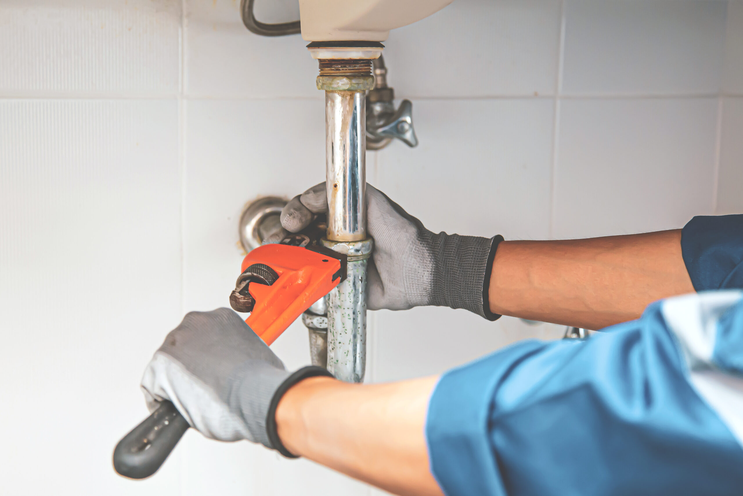 Certified Plumber using a wrench to repair a water pipe under the sink